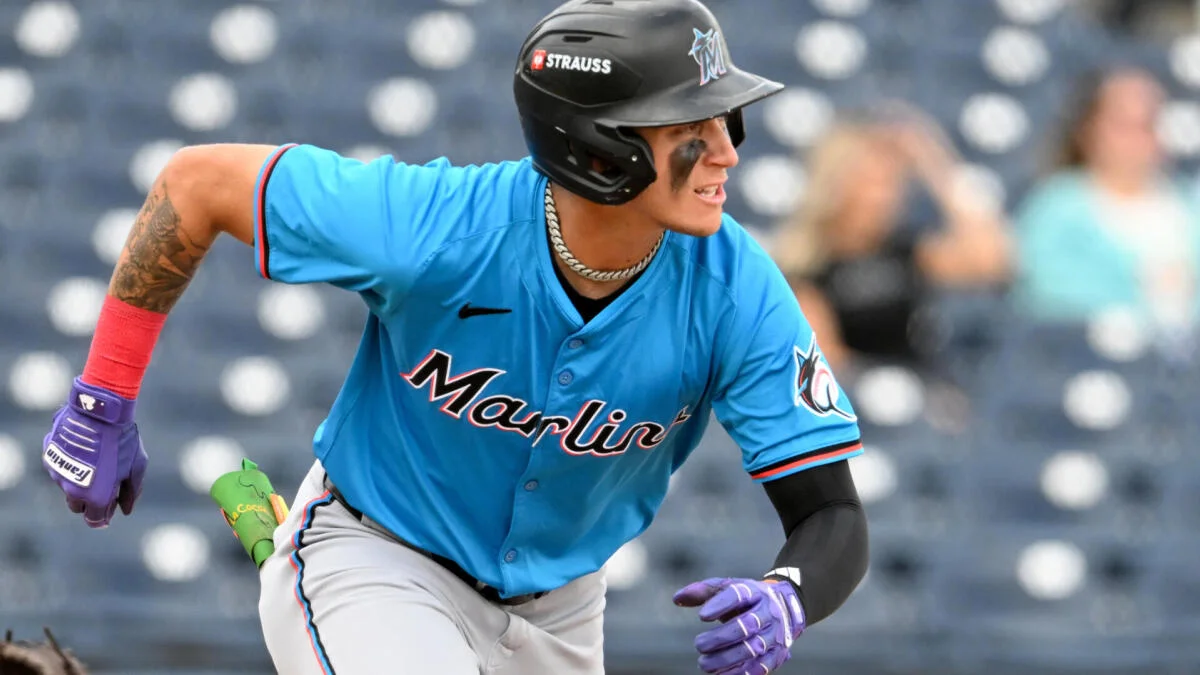 Baseball player in Miami Marlins uniform running while wearing a black batting helmet and purple gloves
