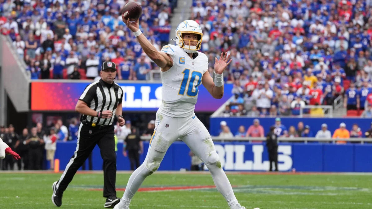 Quarterback in a white number 10 uniform prepares to throw as a referee watches nearby.