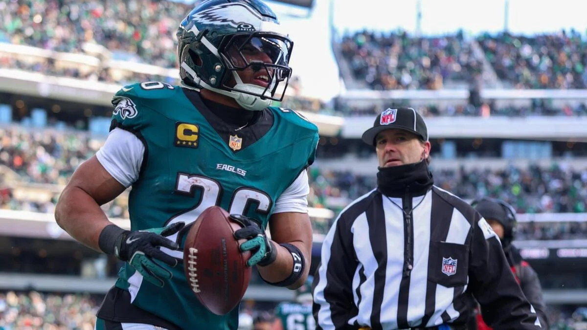 Philadelphia Eagles player in a teal uniform holds a football beside a referee on the field.