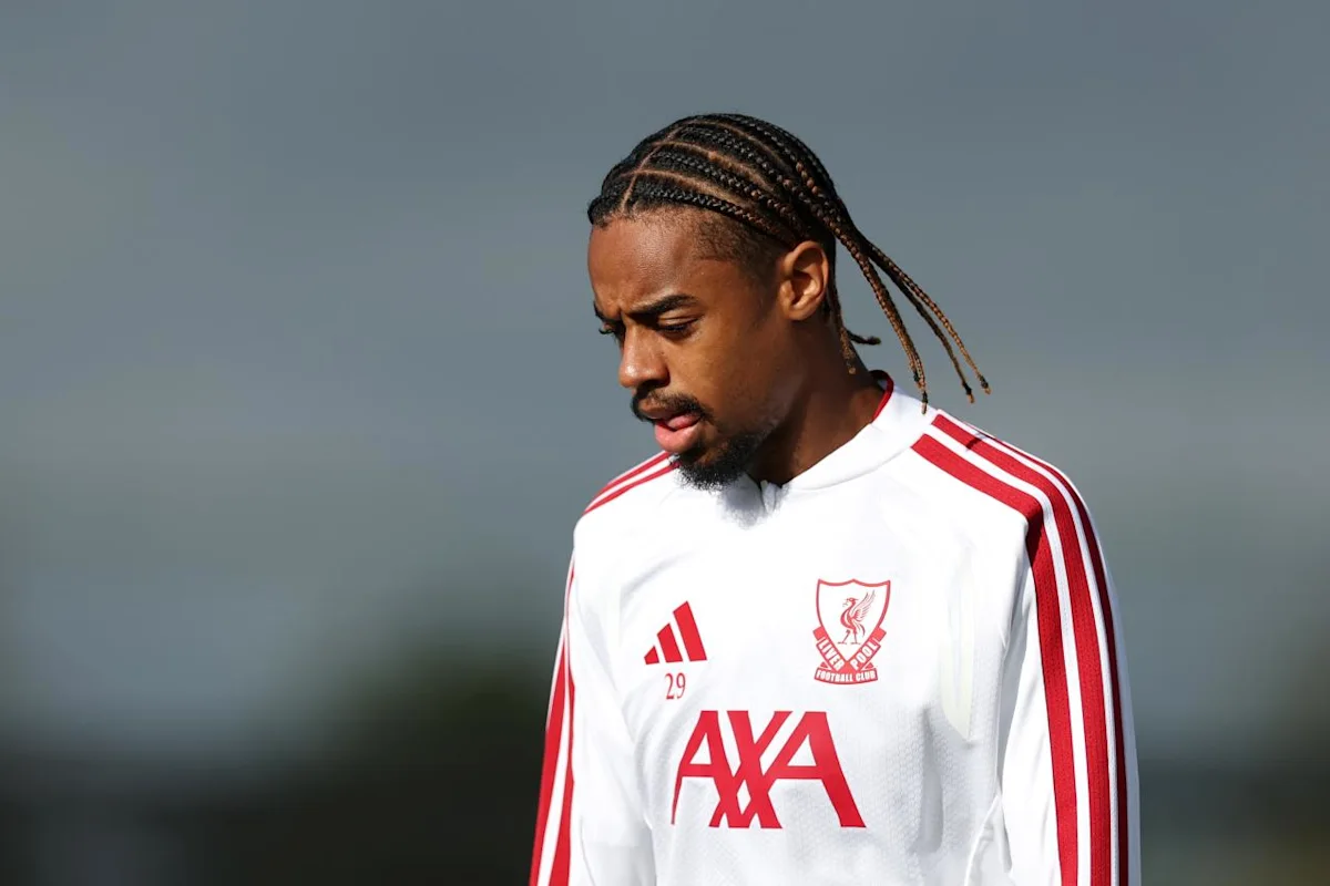 Footballer with braided hair wearing a white Liverpool training shirt with red stripes and logos