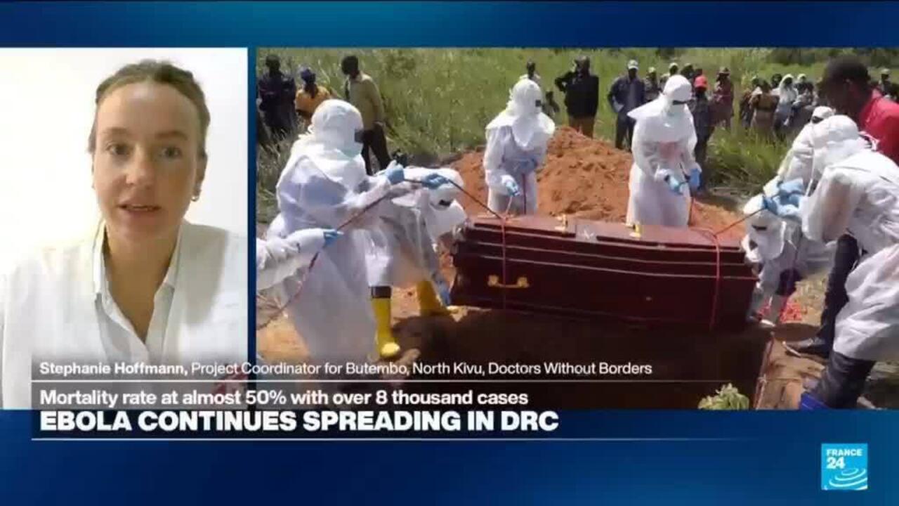 Health workers in protective suits lower a coffin into a grave as onlookers gather; a woman appears in a video interview.