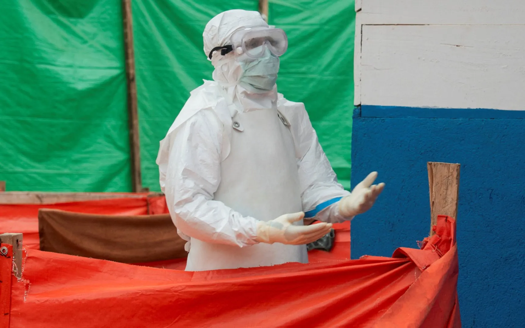 Person in full white protective gear and goggles stands behind red barriers outdoors.