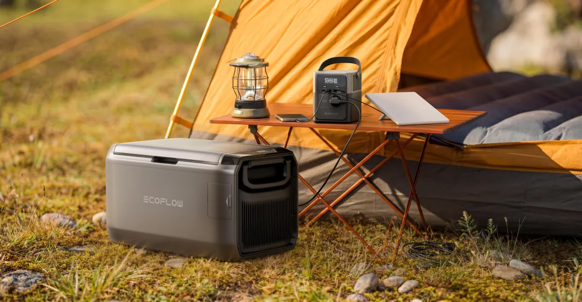 Portable EcoFlow power station beside a camping tent, lantern, laptop, and folding table