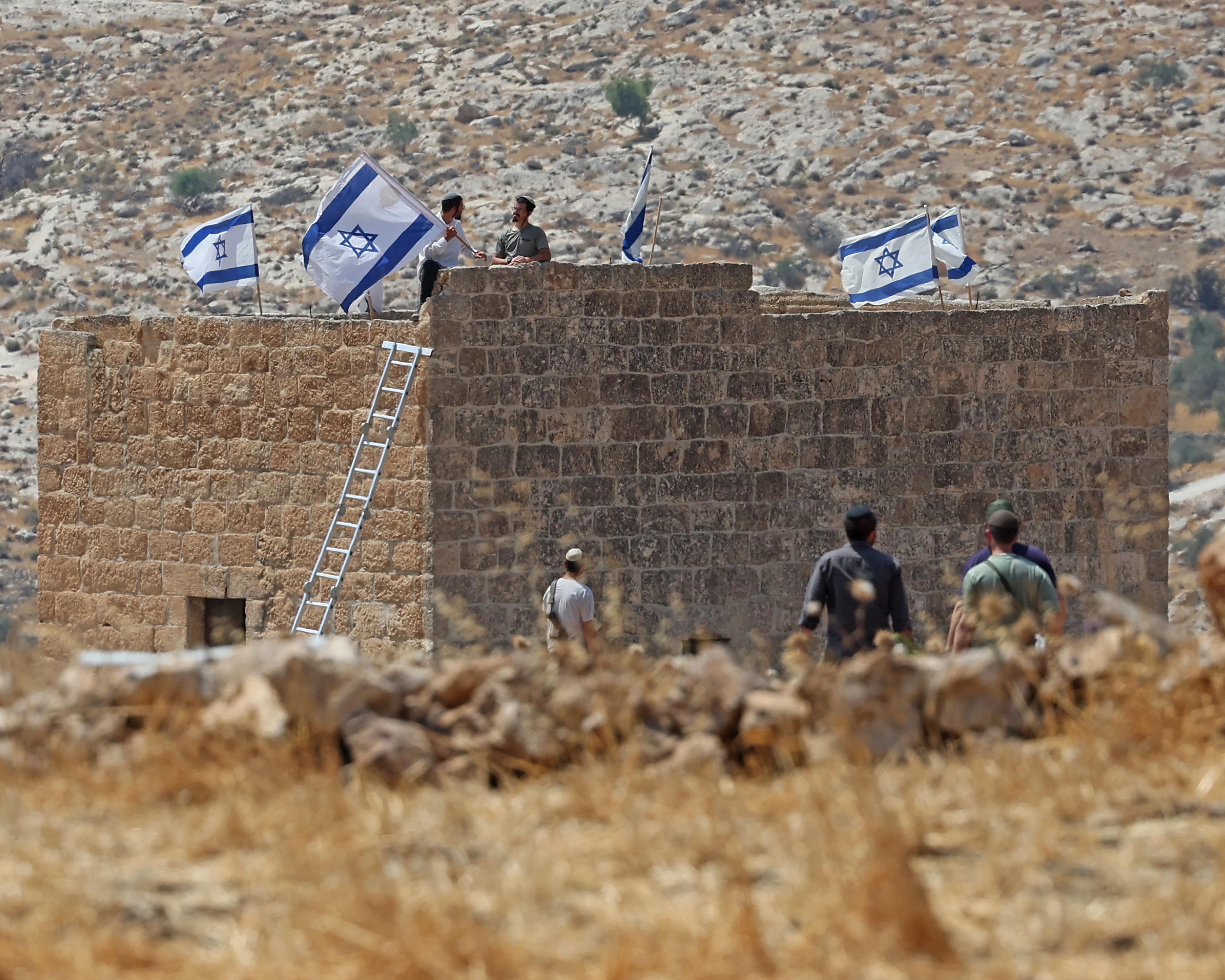 People gather around a stone wall displaying several Israeli flags in a rocky landscape.