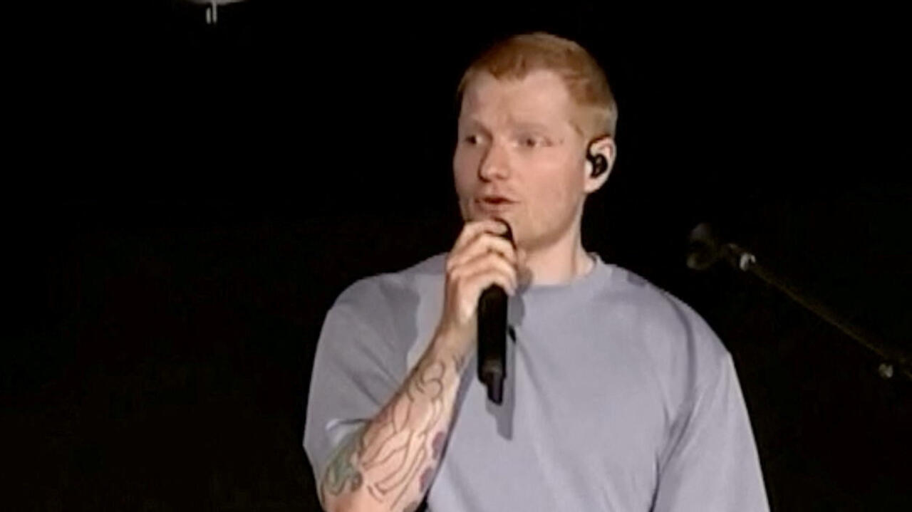 Red-haired singer holding a microphone while performing on a dimly lit stage