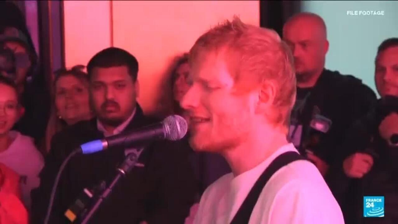Red-haired man sings into a microphone before a crowd, with France 24 branding visible.