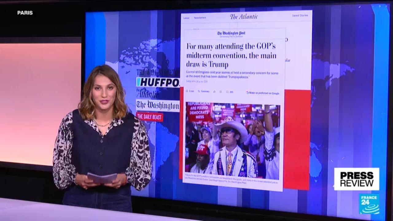News presenter stands beside a screen displaying newspaper coverage of a Republican convention and Trump.