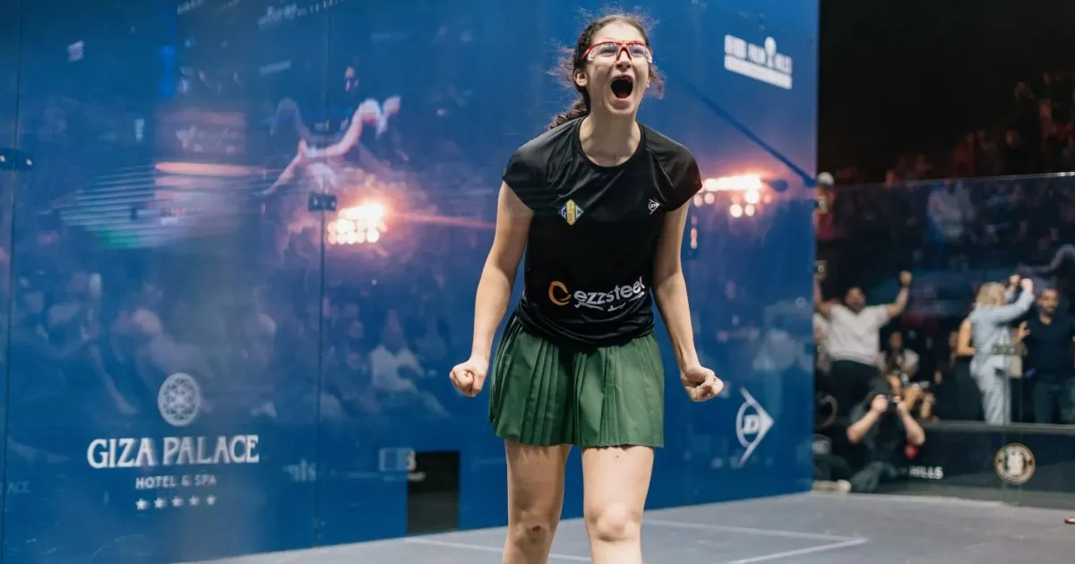 Squash player celebrating on court with clenched fists and cheering spectators behind her