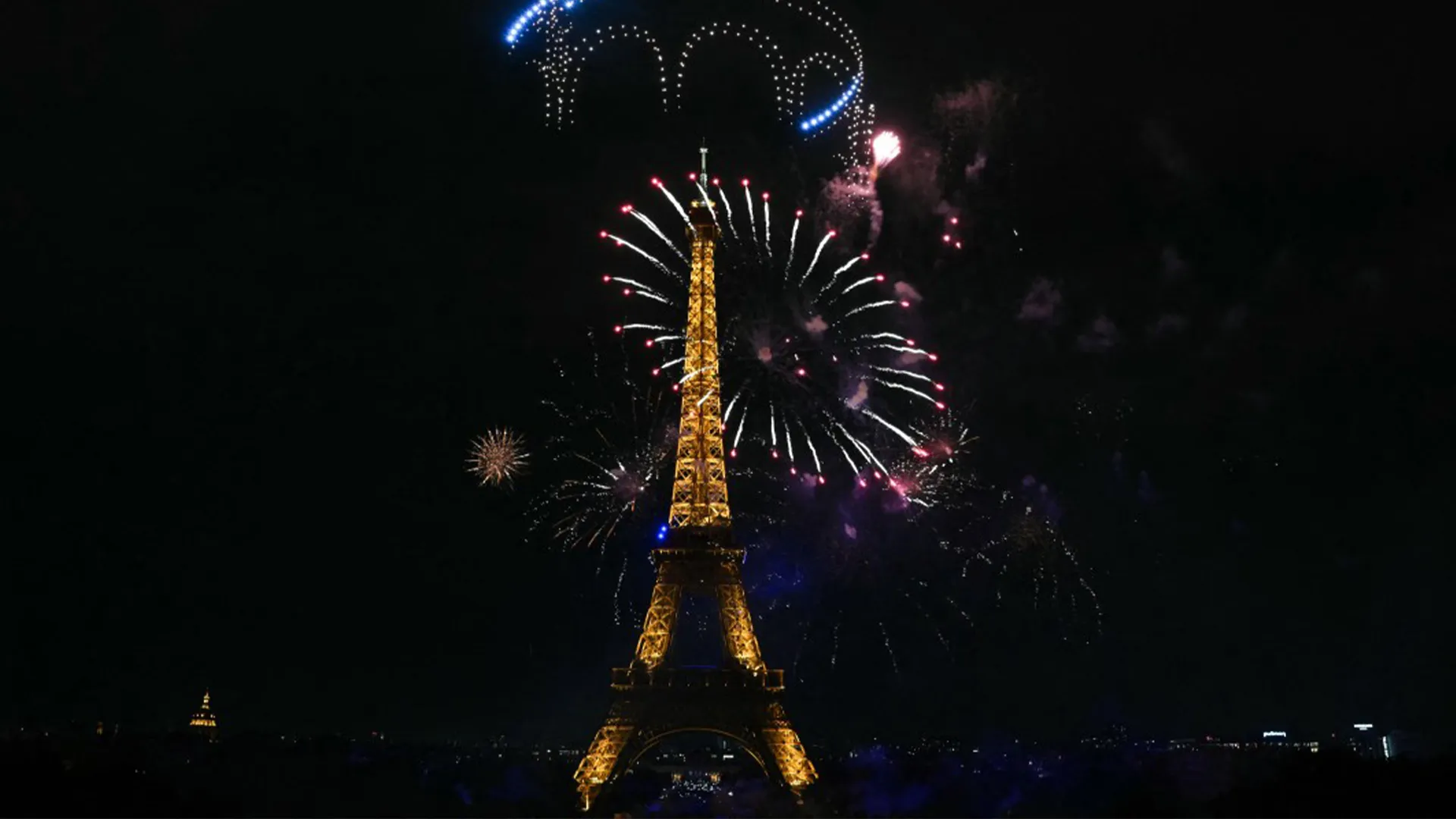 Eiffel Tower illuminated during a nighttime fireworks display against a dark sky