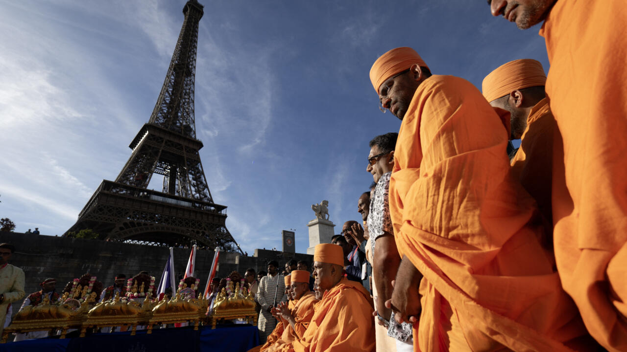 Orange-robed Hindu devotees gather beside the Eiffel Tower during a ceremonial procession.