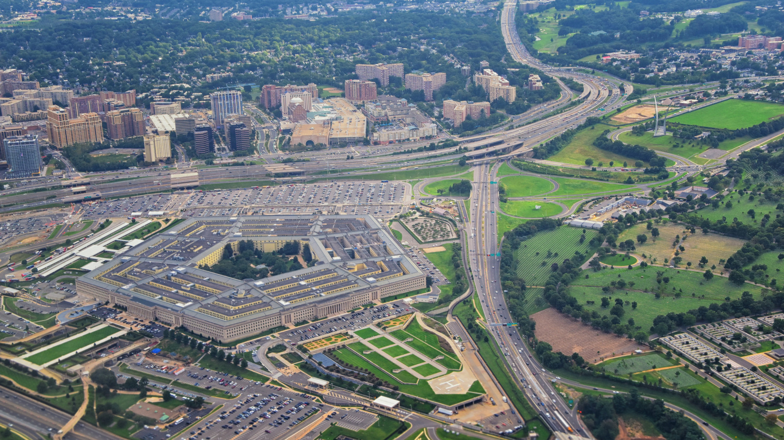 Aerial view of a large Pentagon-shaped building beside highways, parking lots, and surrounding green spaces.