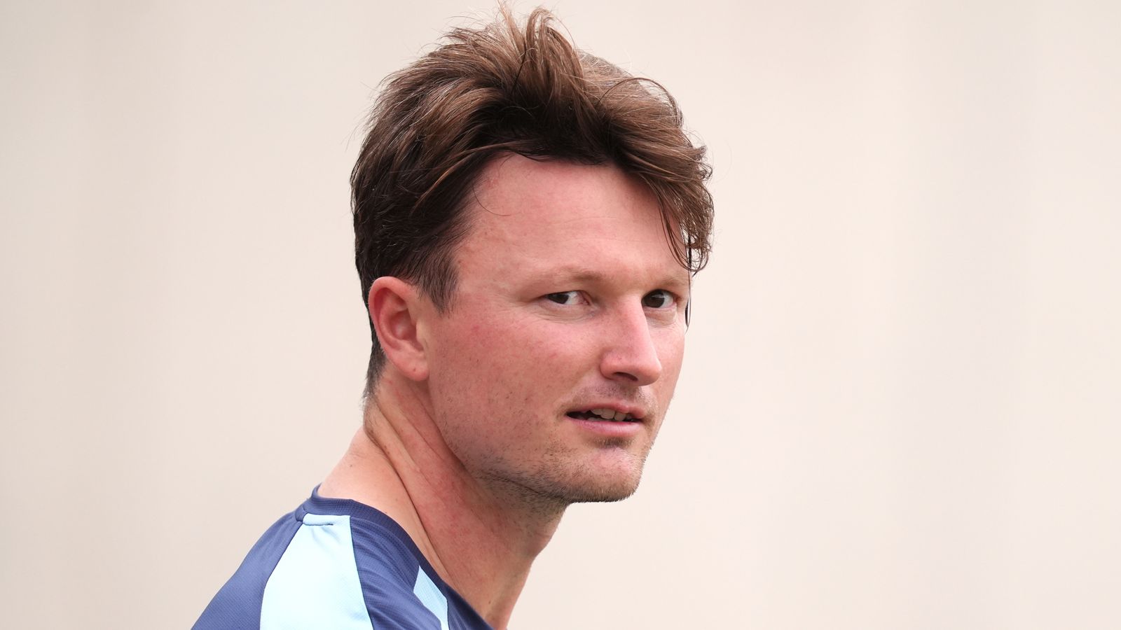 Close-up of a male cricketer in a blue training shirt looking over his shoulder