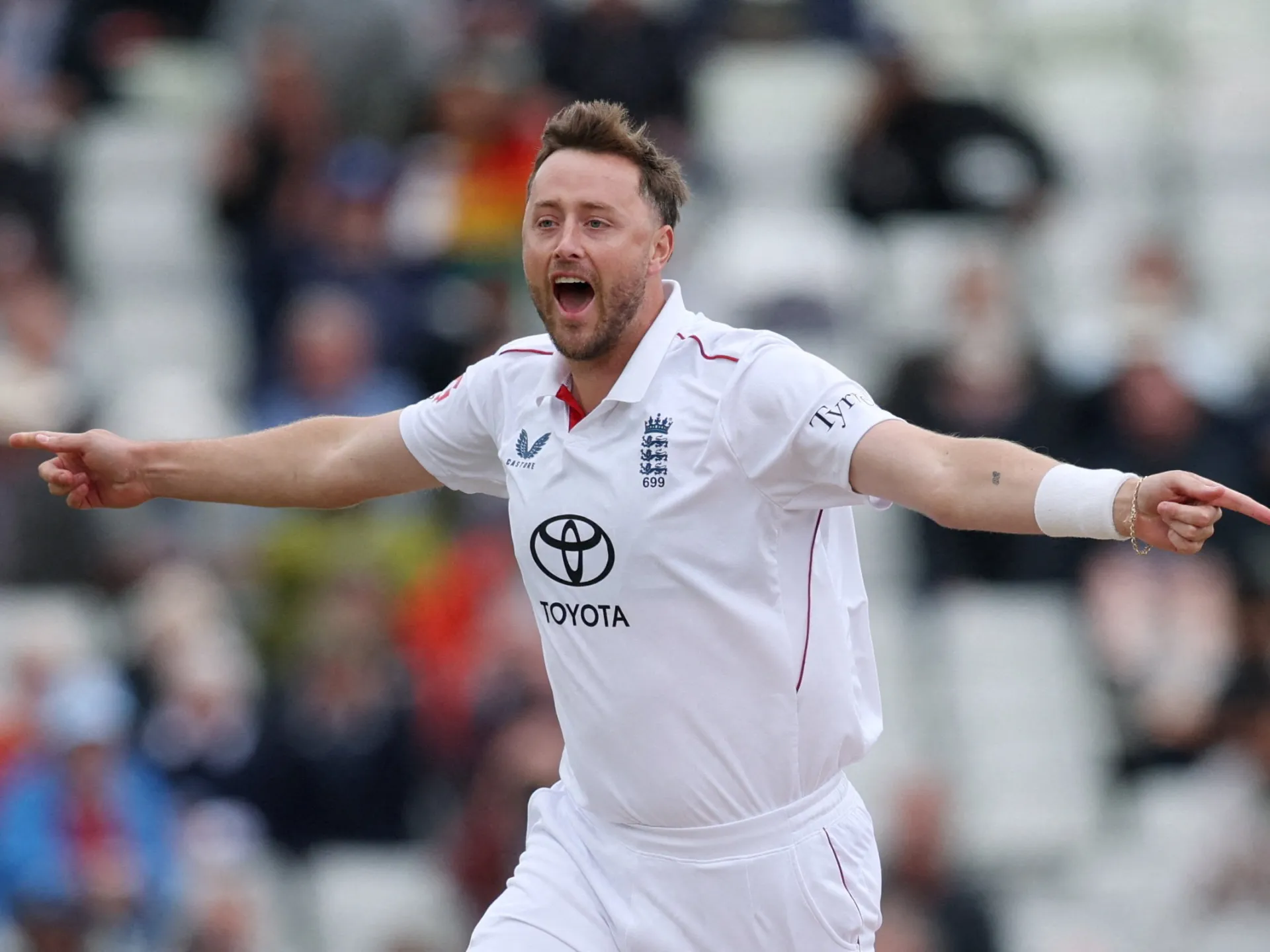 England cricketer in white kit celebrates with arms outstretched before a blurred crowd
