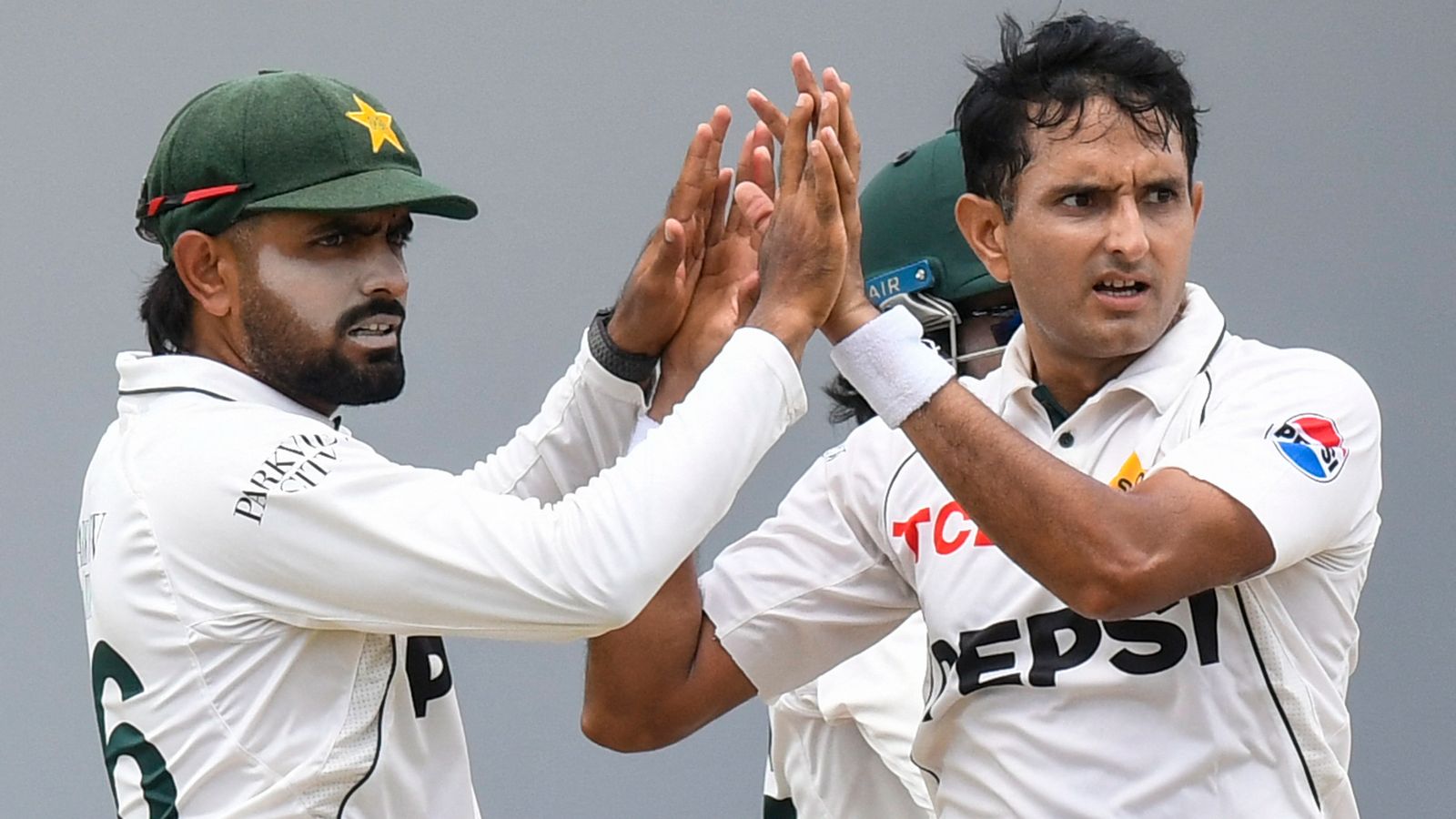 Pakistan cricketers in white Test uniforms celebrate with raised hands during a match.