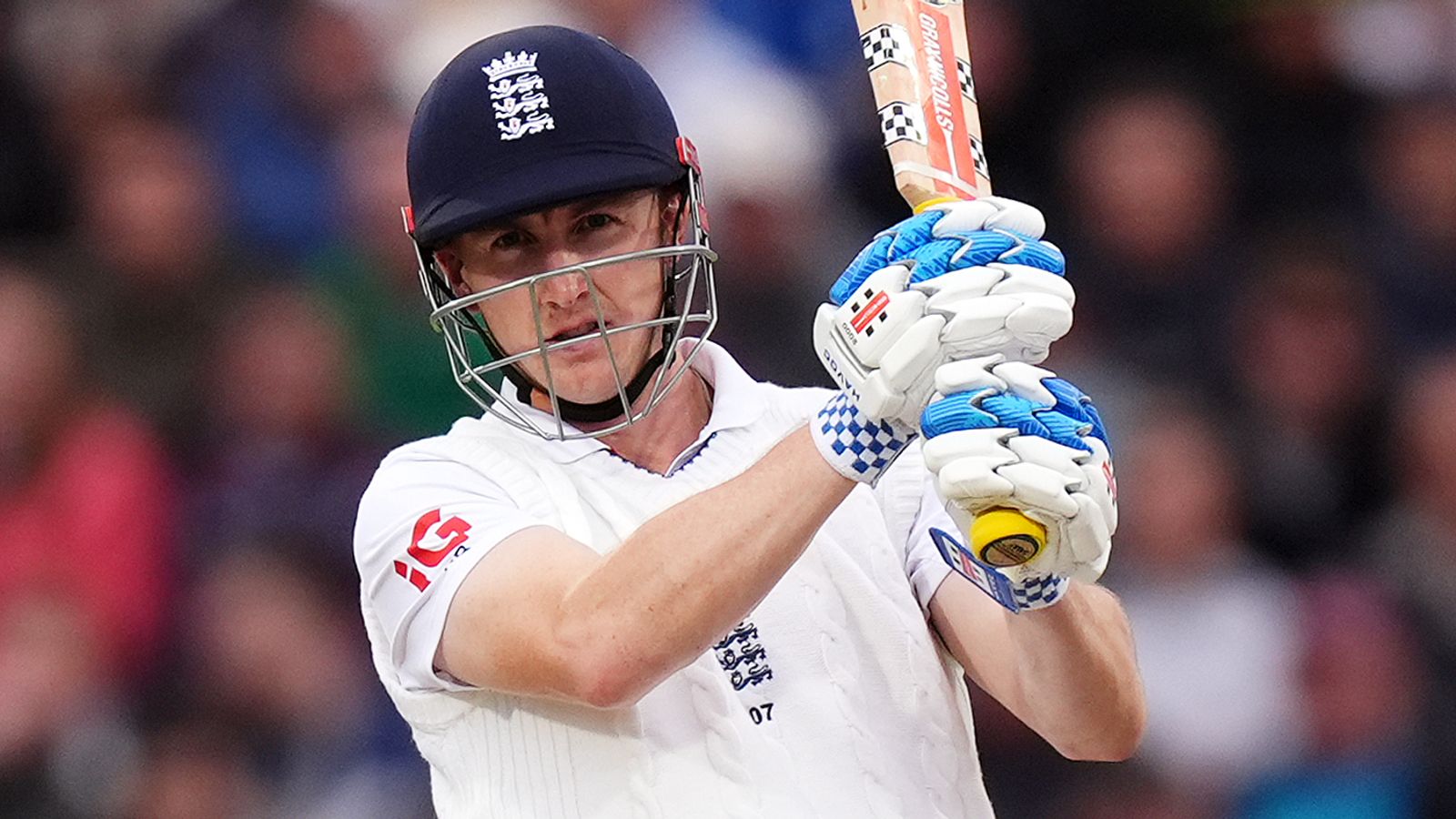 England batsman in helmet and white kit raises his bat during a cricket match