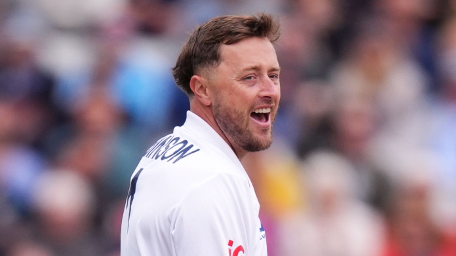 England cricketer in white Test shirt reacts with mouth open before a blurred crowd