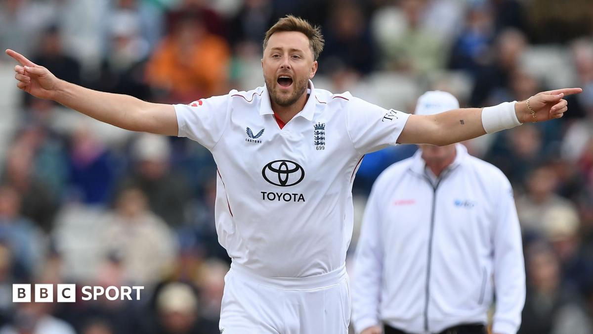 England cricketer in white kit stands with arms outstretched during a match
