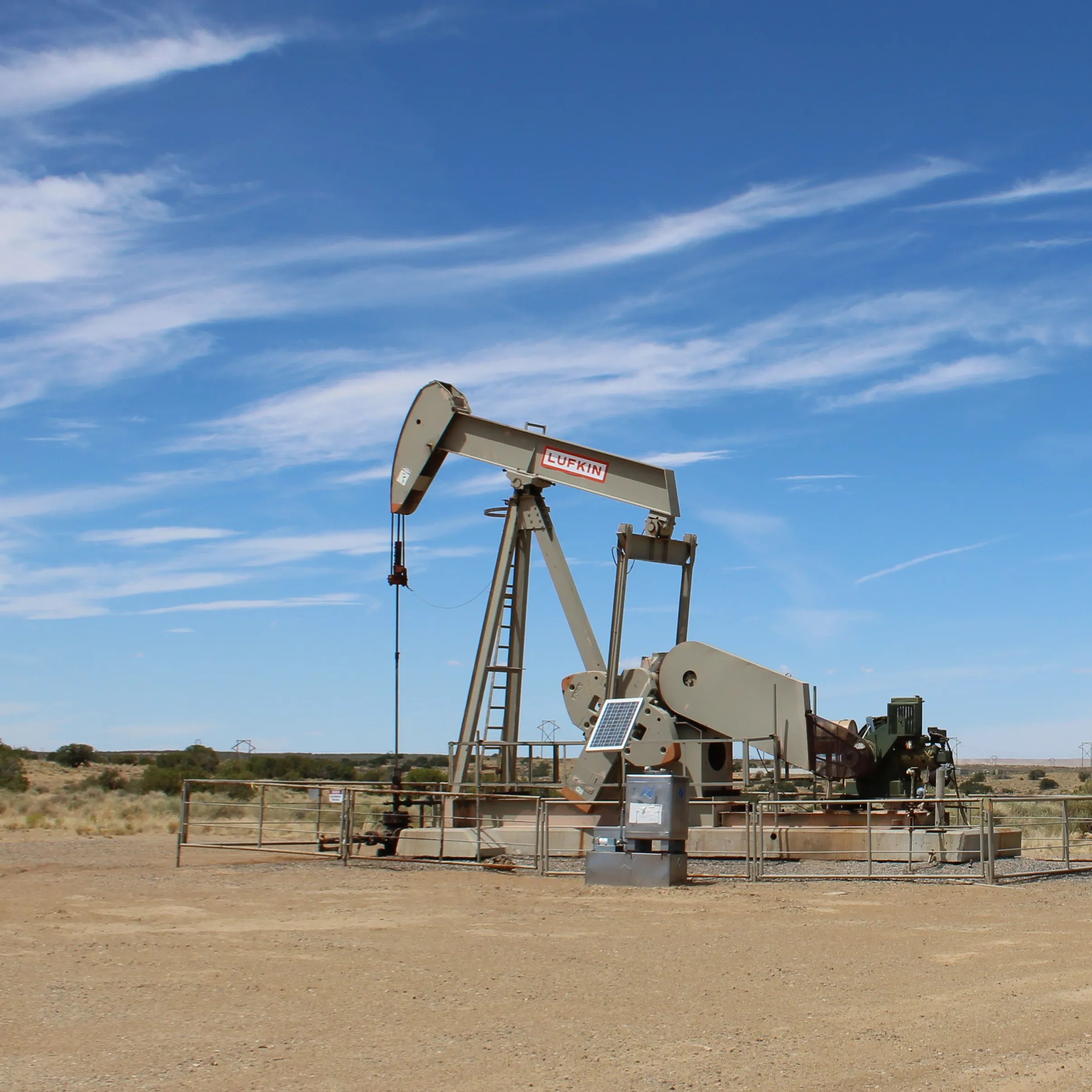 Oil pumpjack operating in a dry landscape beneath a blue, cloud-streaked sky.