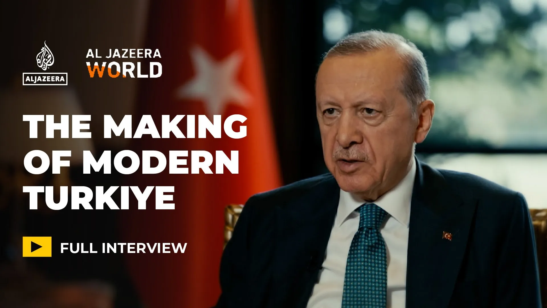 Man in suit seated beside a Turkish flag, with interview title text displayed on screen.