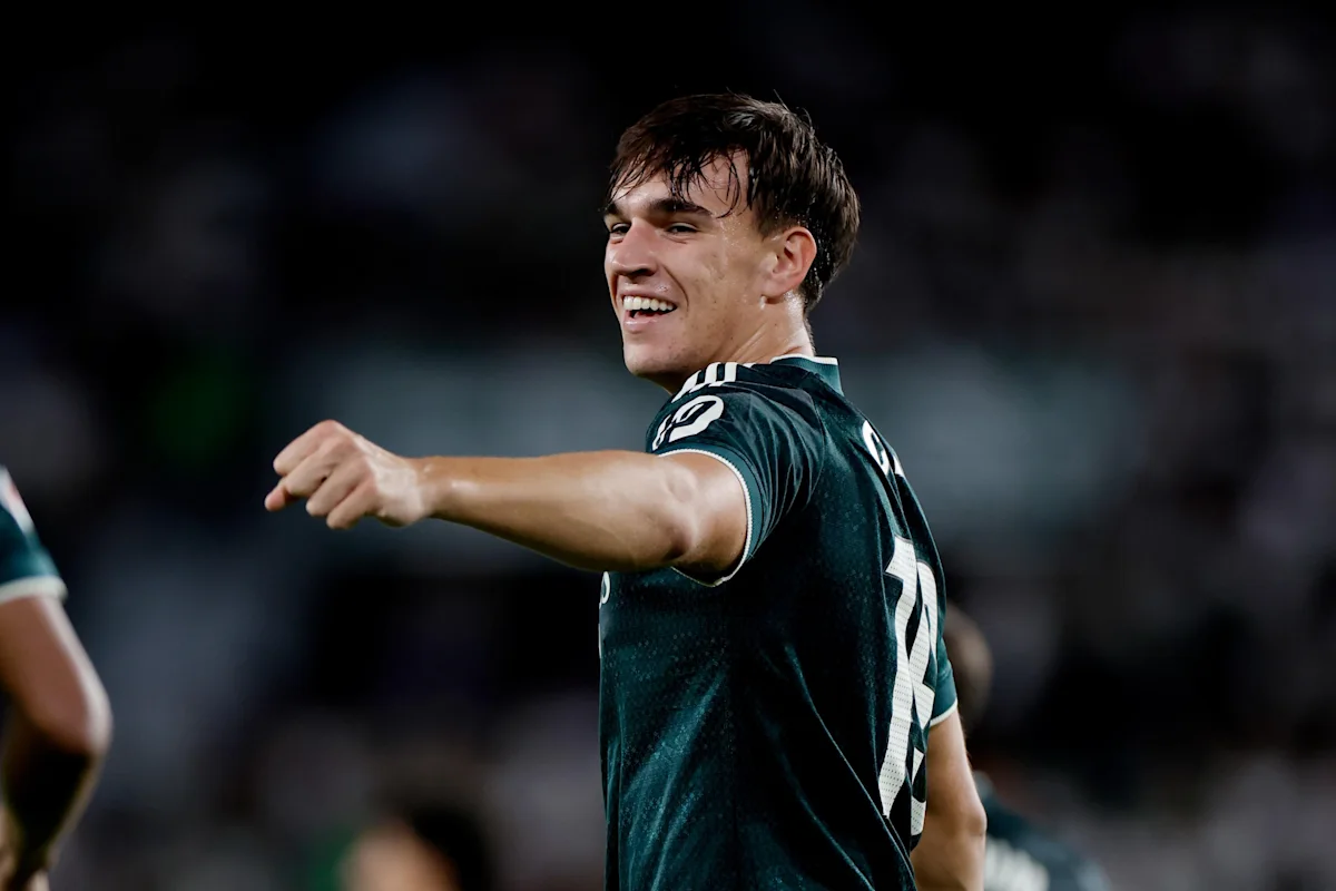 Smiling football player in dark green jersey points while turning toward the field.
