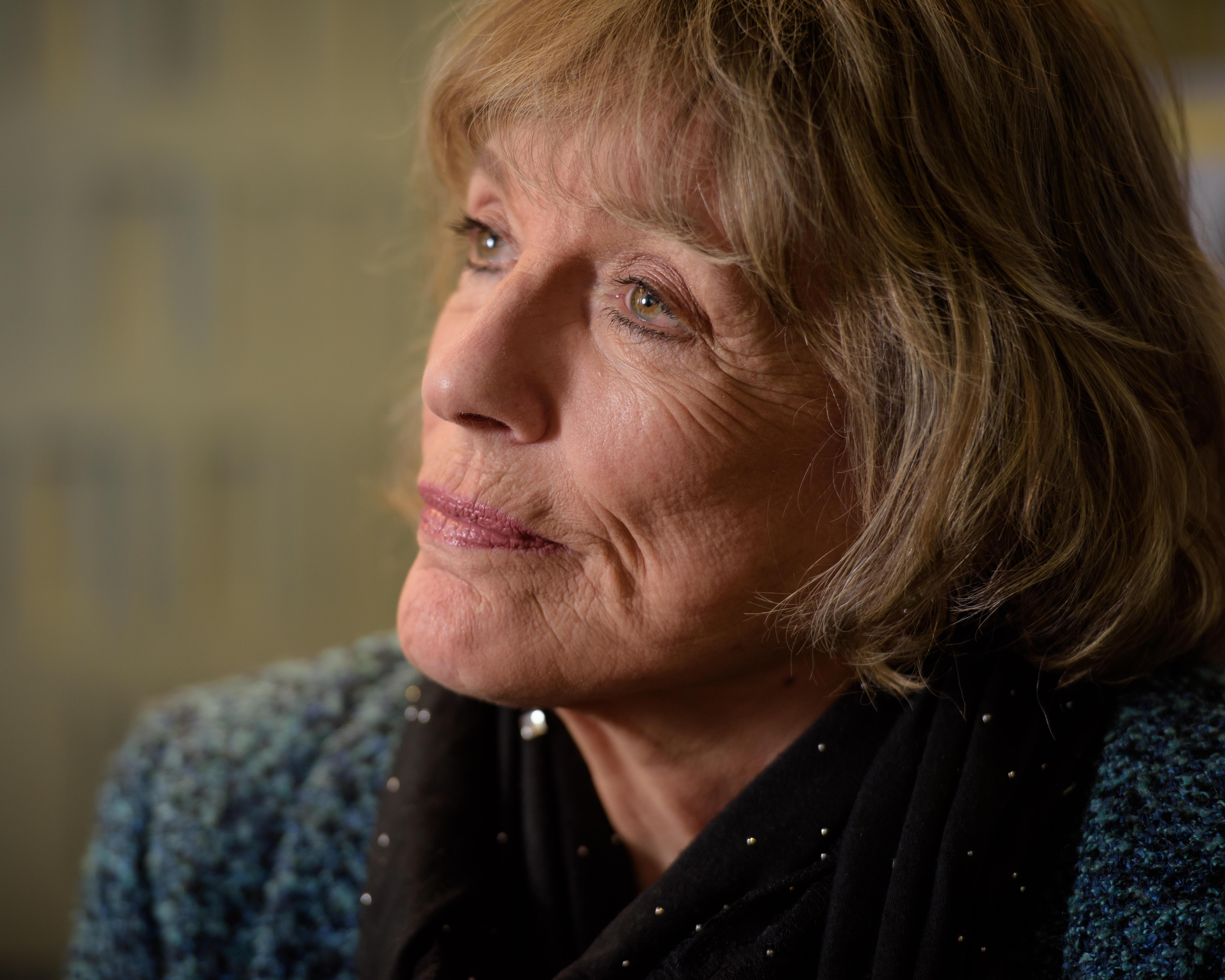 Close-up portrait of an older woman with short light-brown hair looking thoughtfully to the left.