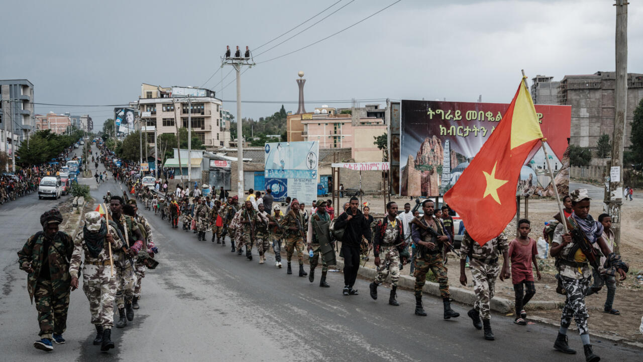 Armed people walk along a city road, with a large red flag bearing a yellow star.