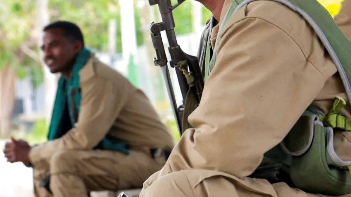 A seated man in tan clothing and a teal scarf, with a large tan-clad figure in the foreground.