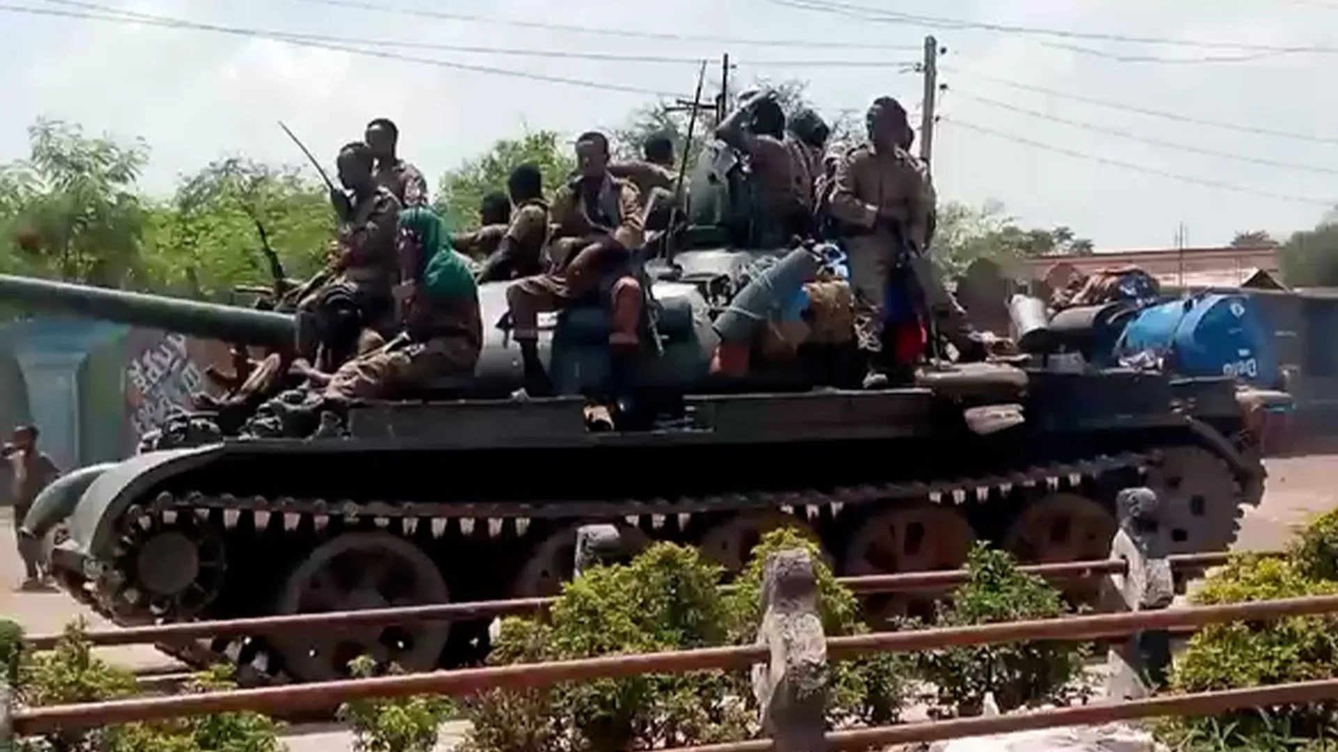 Soldiers ride atop a tracked military vehicle carrying equipment along a roadside.