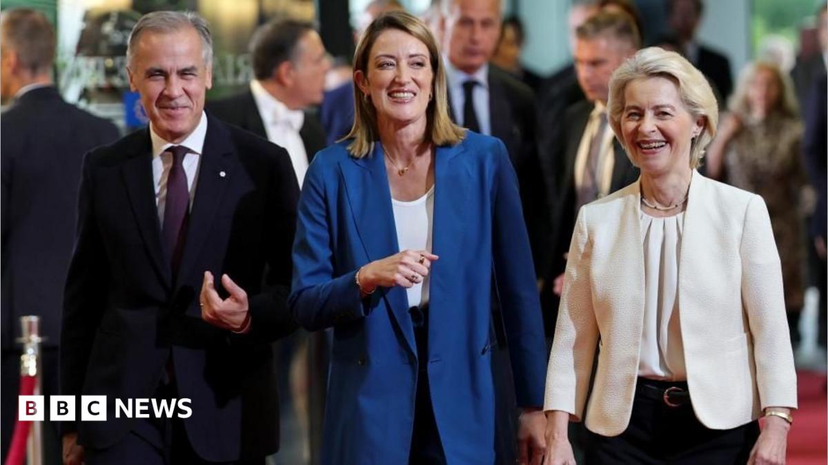 Three formally dressed officials walk together, smiling, during a public event.