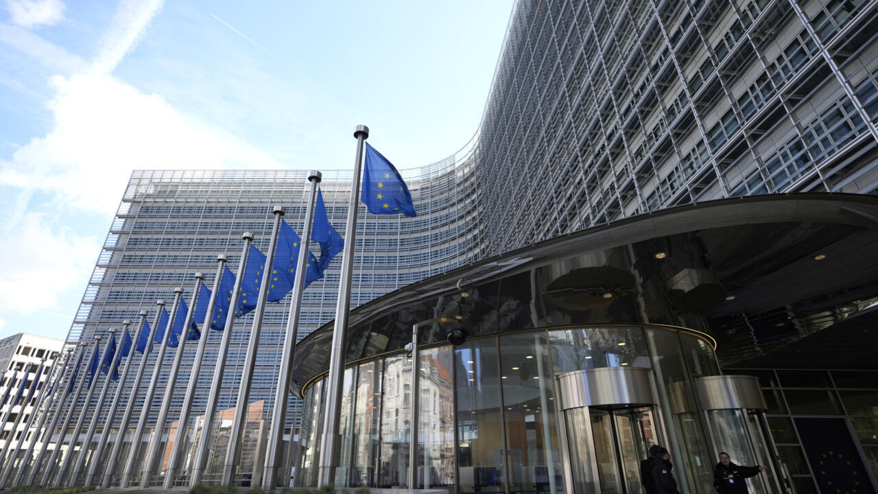 European Union flags flying outside a modern institutional building beneath a partly cloudy sky
