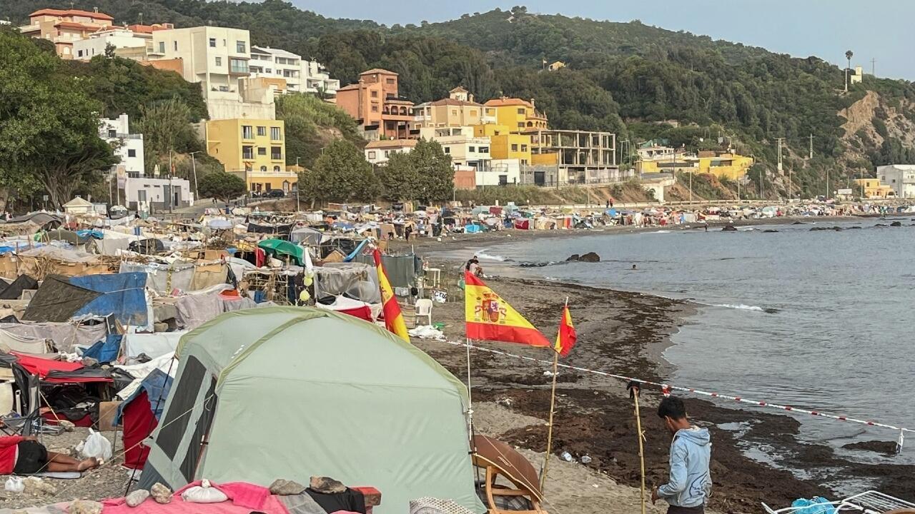 Coastal settlement with tents, boats, Spanish flags and hillside apartment buildings beside the sea.