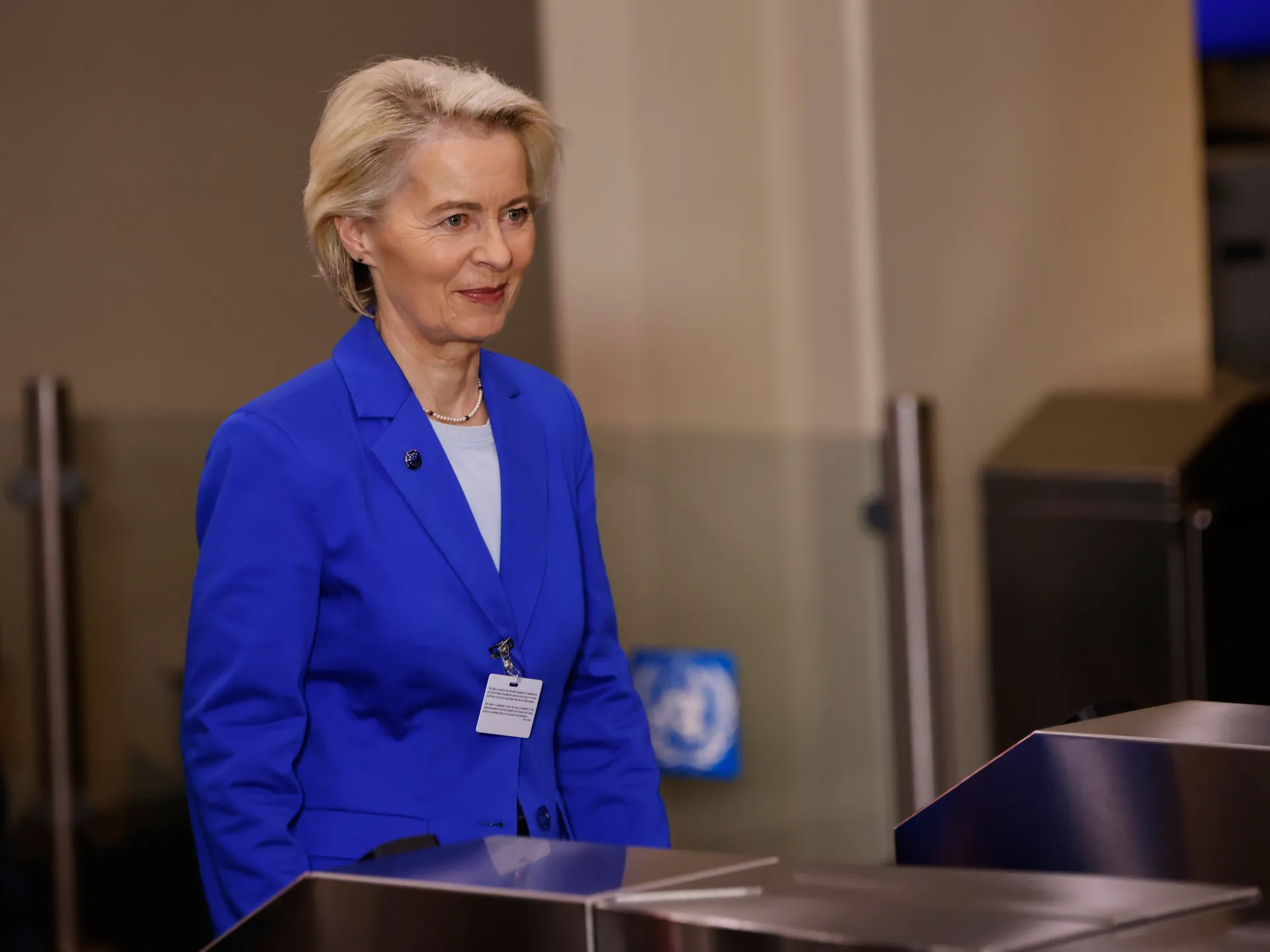 A blonde woman in a blue blazer stands behind a lectern in an indoor venue.