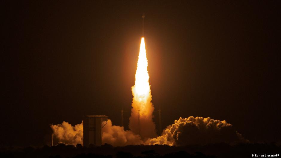 Rocket launches vertically at night, surrounded by bright flames, smoke, and illuminated clouds.