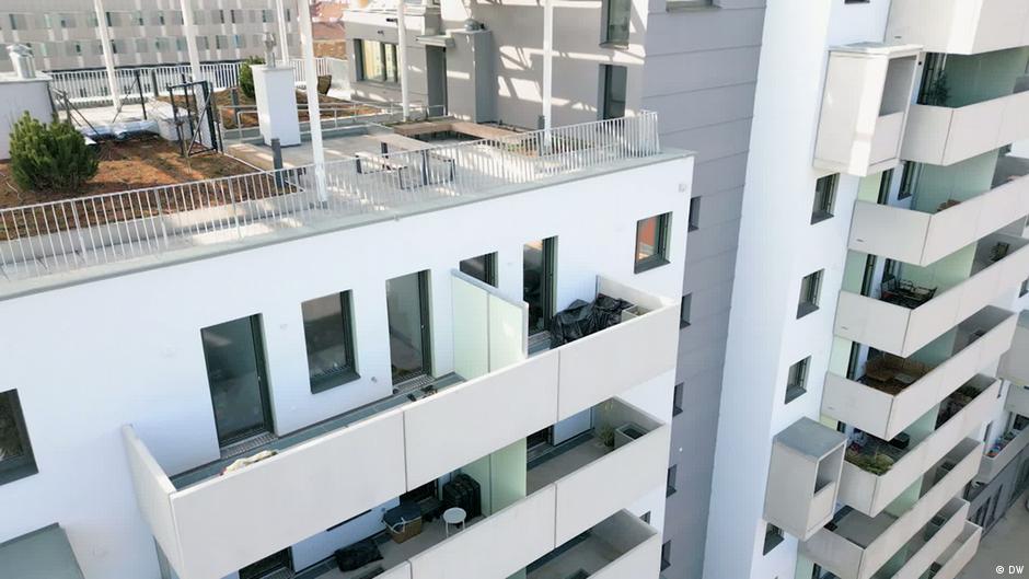 Modern apartment building with white balconies and a shared rooftop terrace, photographed from above.