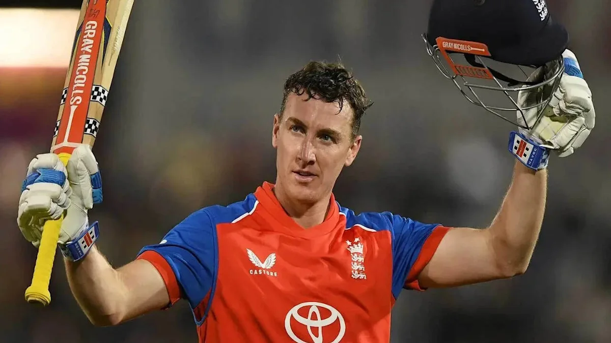 Cricketer in England jersey raises bat and helmet in celebration during a match