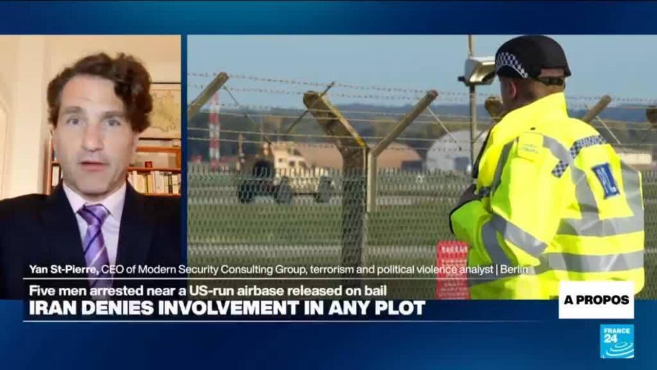 Split-screen shows a suited man speaking beside a police officer at a fenced airfield.