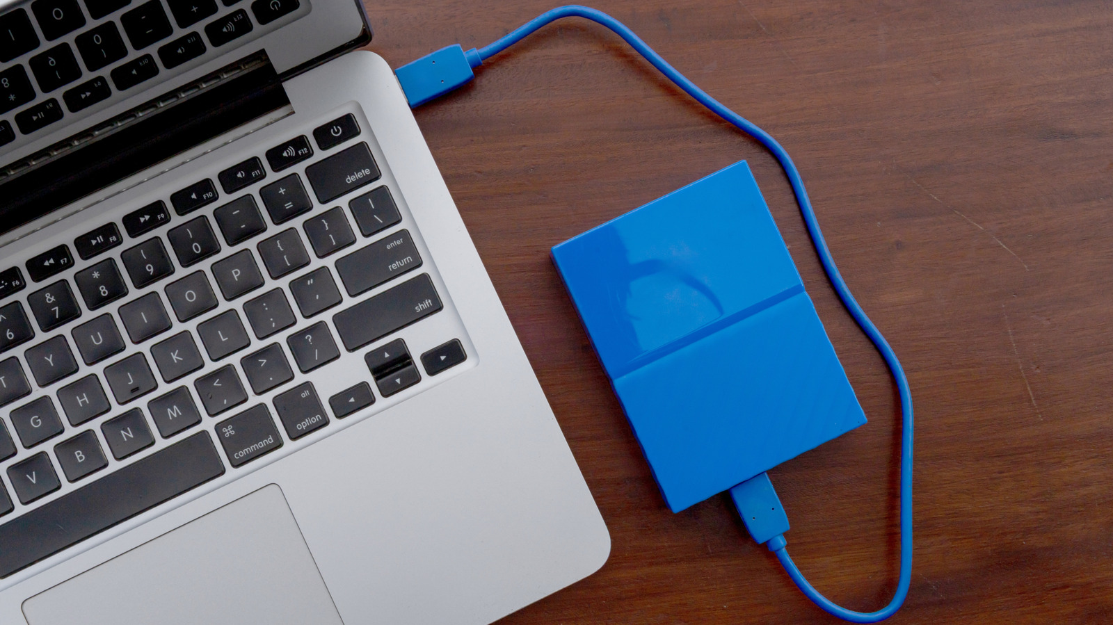 Laptop connected to a blue external hard drive by USB cable on a wooden desk.