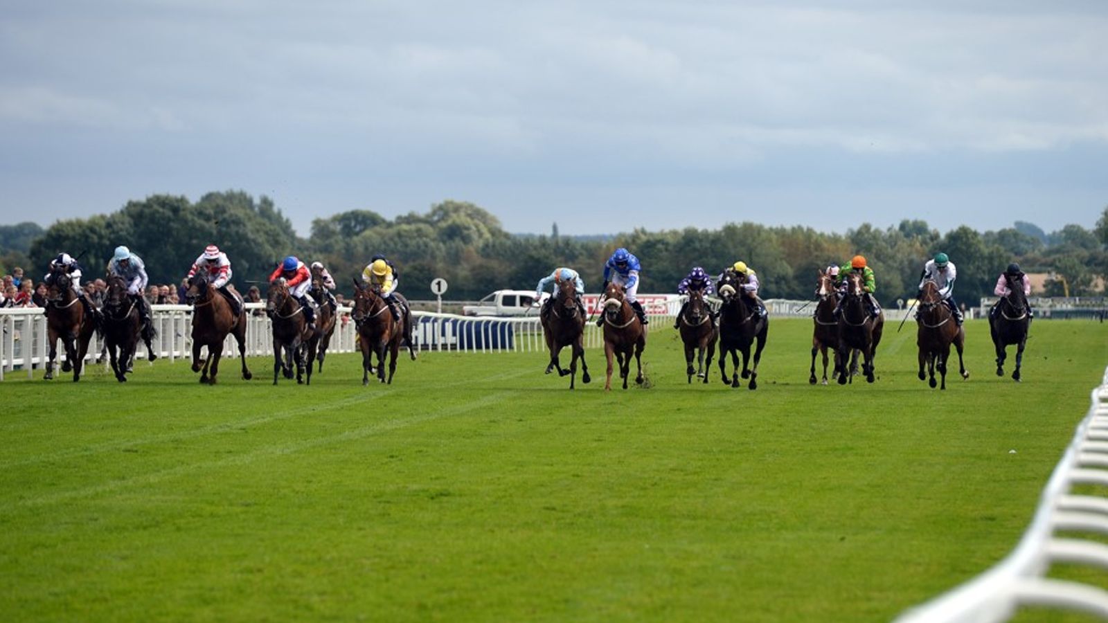 Jockeys in colorful silks race horses across a green turf course beside white rails.