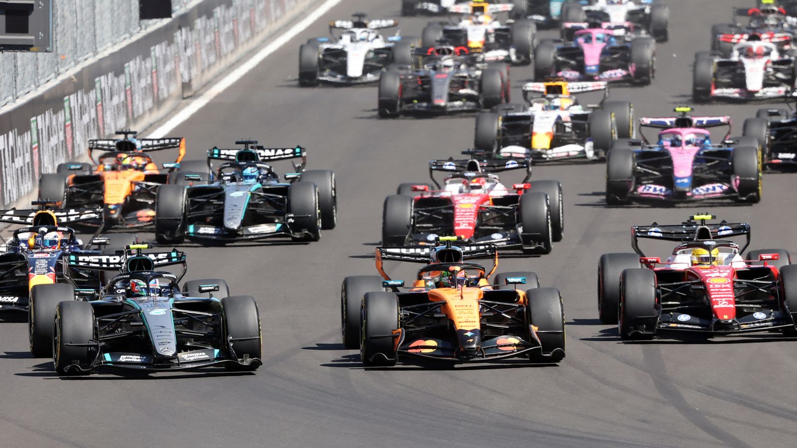 Formula One cars race closely together on a circuit during a packed opening-lap scene