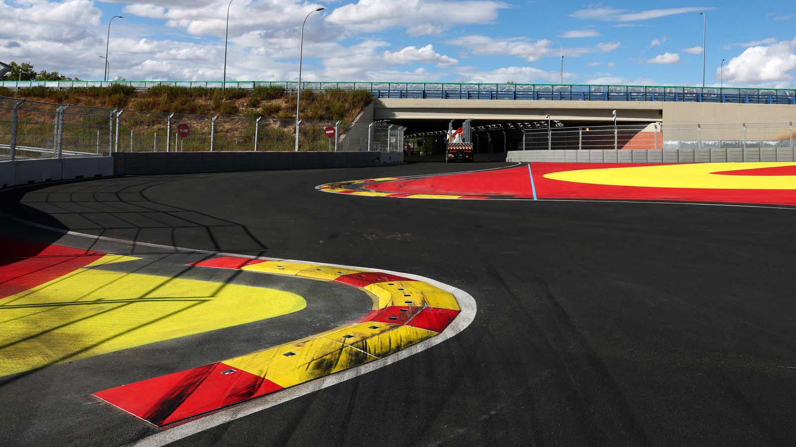 Empty race circuit chicane with red and yellow kerbs beside an underpass and safety barriers