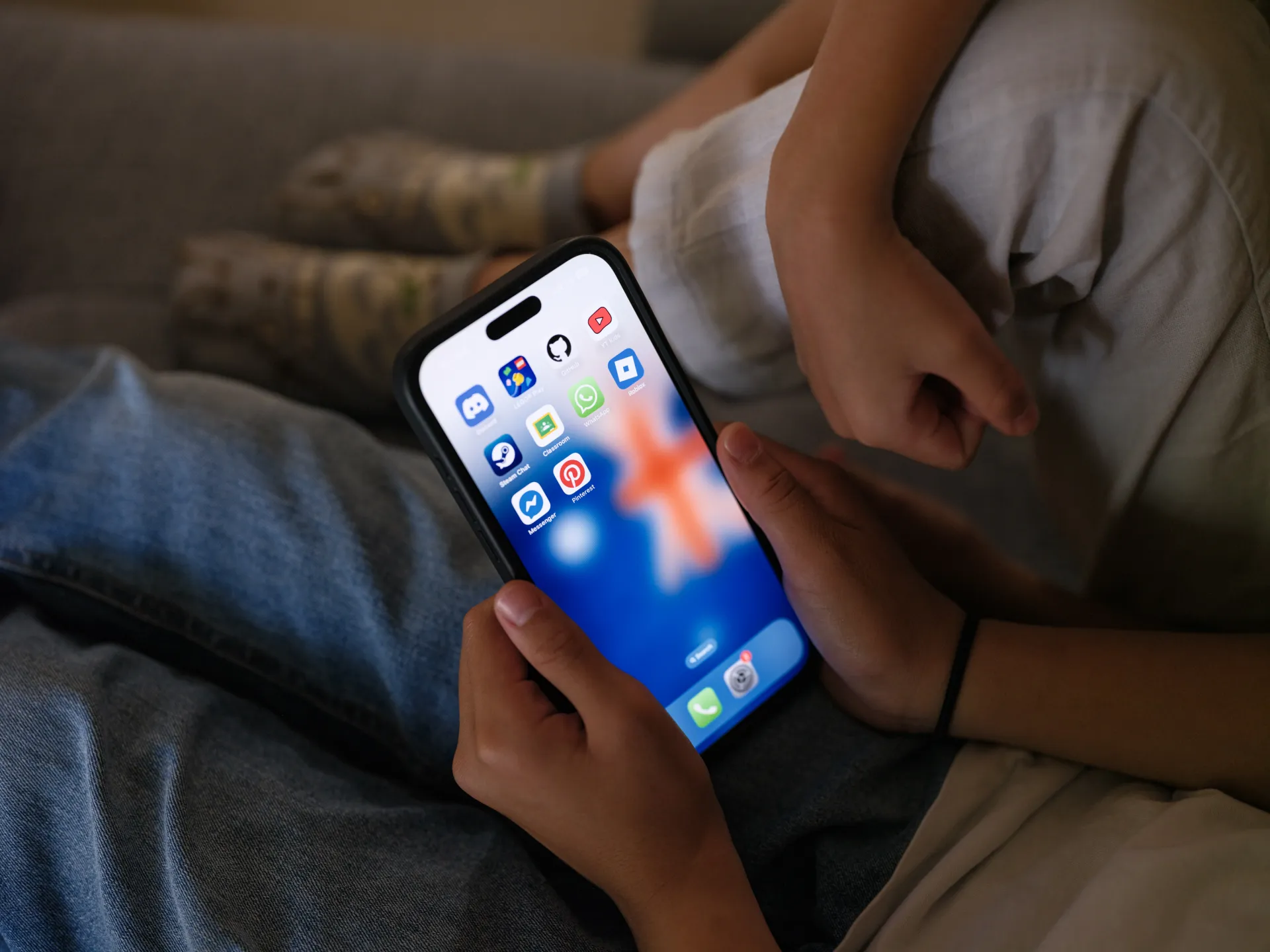 A person holds a smartphone displaying social media app icons while seated on a couch.