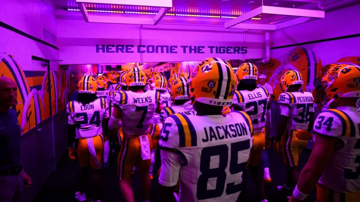 Football players in purple-lit uniforms gather in a stadium tunnel before entering the field.