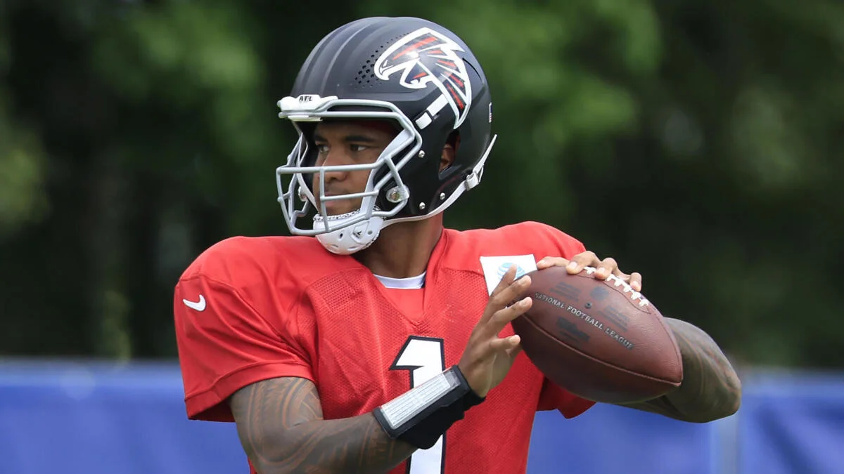 Football player in Falcons helmet and red jersey holding a football during practice