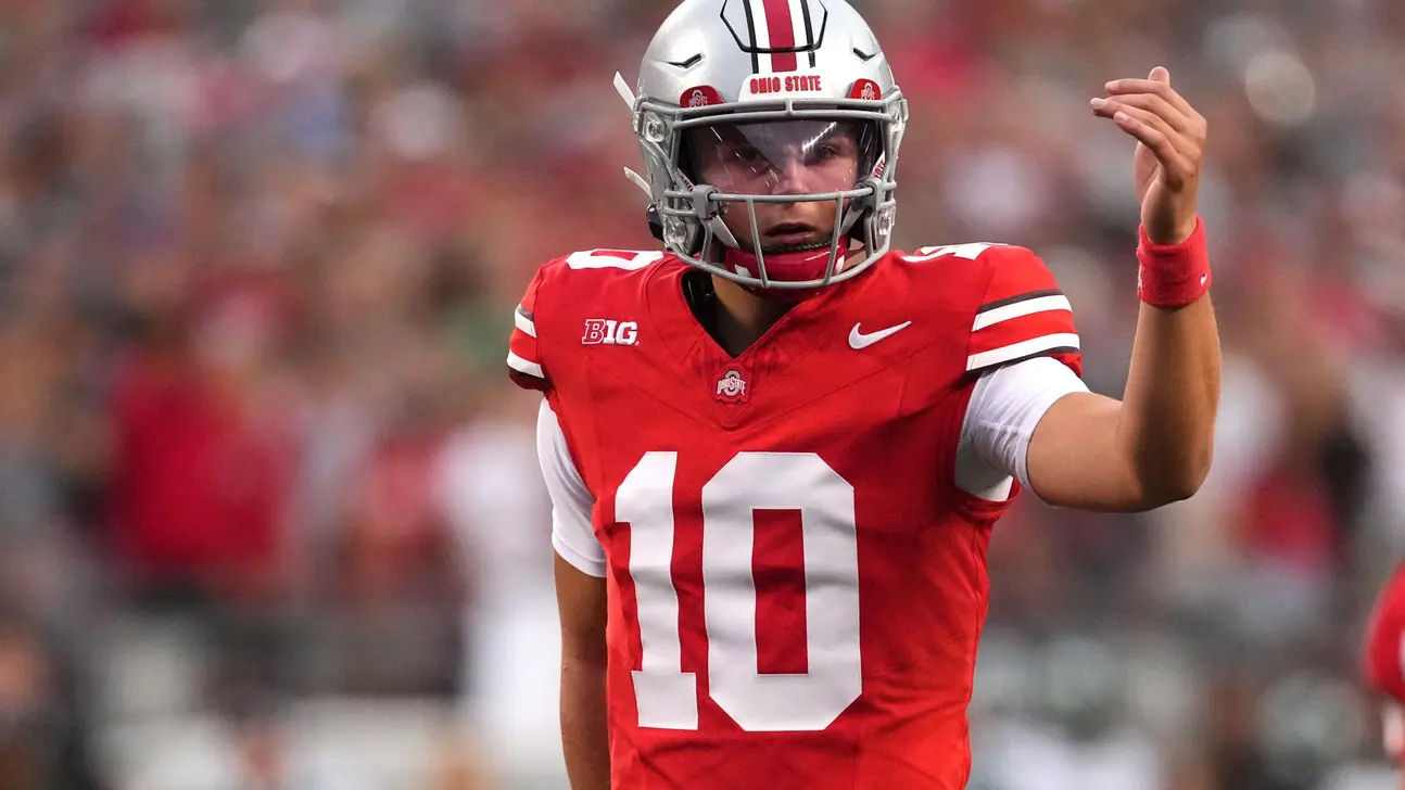 Ohio State football player in red uniform and helmet raises his hand during a game