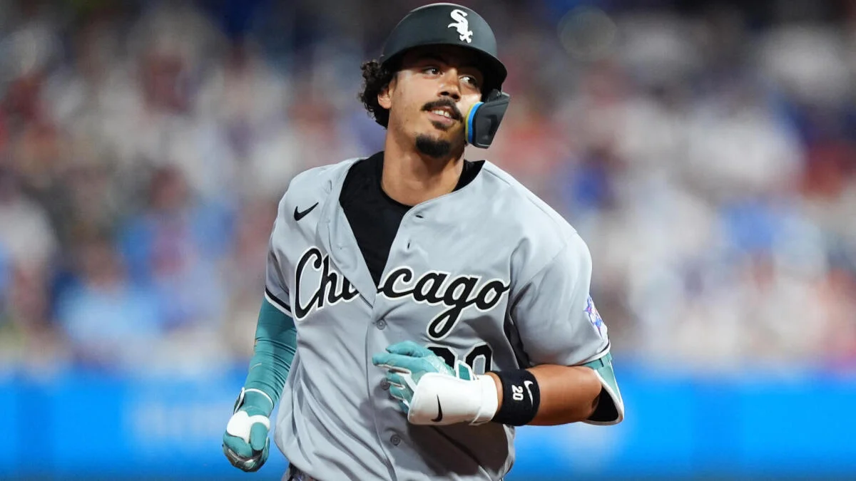 A Chicago White Sox player in a gray uniform runs across the field wearing a batting helmet and teal gloves.