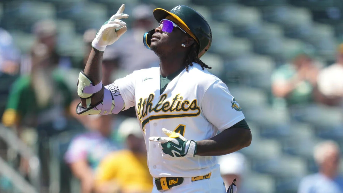 Baseball player in an Athletics uniform gestures upward while running on the field.