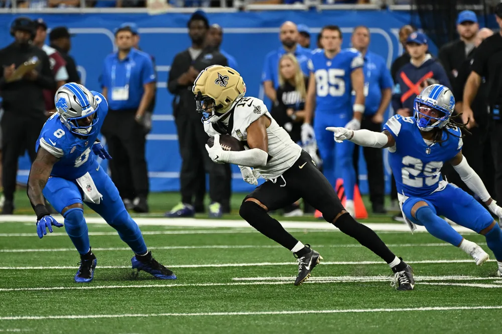 Football player in white runs with the ball between two defenders in blue uniforms.