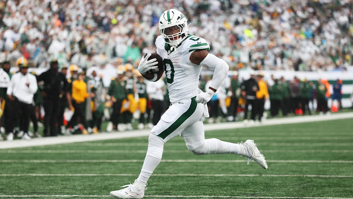 Football player in a white and green uniform runs with the ball on the field.