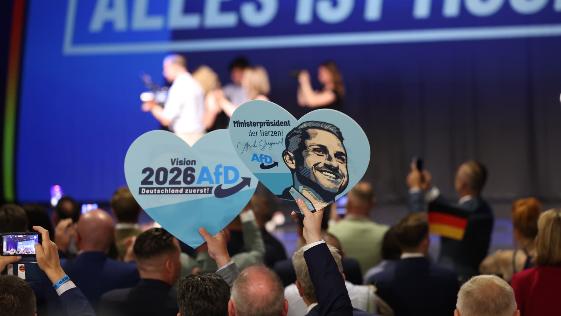 Crowd holds heart-shaped AfD signs toward a stage during a political event.