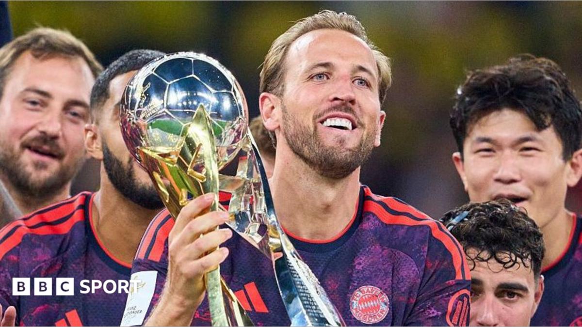 Footballer holding a trophy while teammates celebrate around him in team jerseys